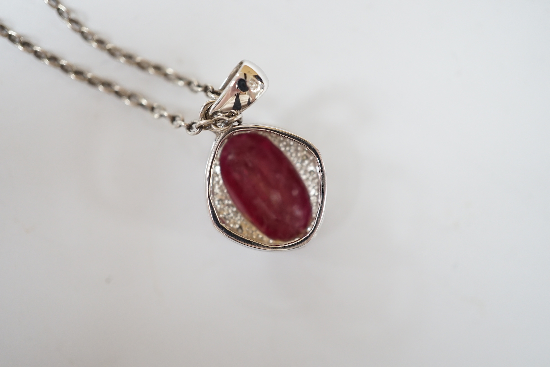 A modern 18ct white gold, ruby and diamond set oval cluster pendant, 24mm, on a white metal chain.